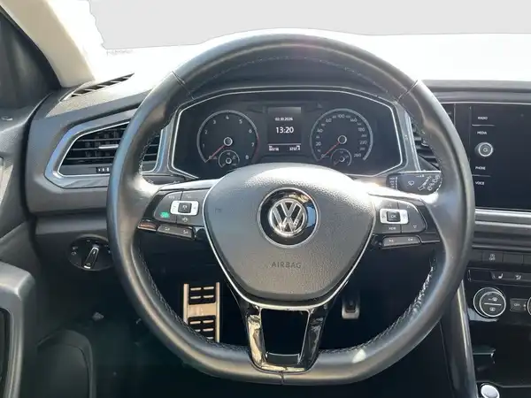 Eine Innenaufnahme des Fahrzeugs VW T-ROC, zeigt das Lenkrad und das Armaturenbrett.