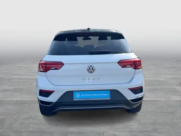 Rückenansicht eines weißen VW T-ROC, mit Händlerlogo im Bild.