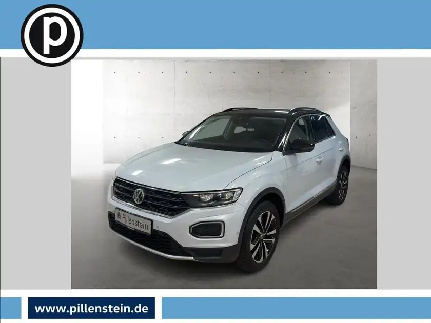 Das Bild zeigt einen weißen VW T-Roc, aufgenommen von vorne. Das Händlerinformationslogo ist sichtbar und es sind markante Texteinblendungen vorhanden.