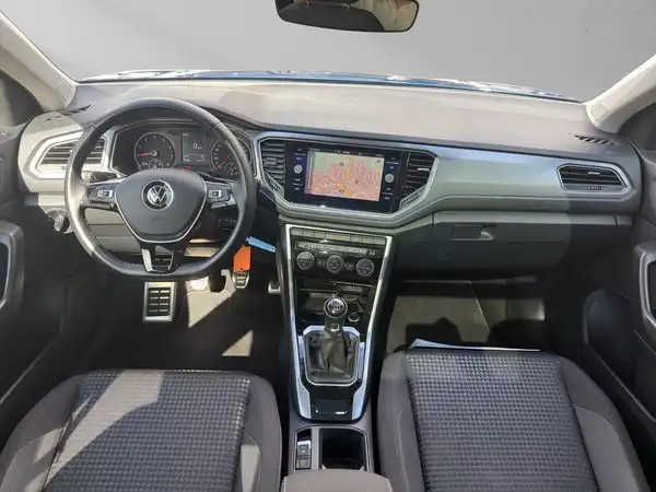 Das Bild zeigt das Innere eines VW T-Roc mit einem grauen Stoffinterieur und einem Navigationsgerät auf dem Armaturenbrett.