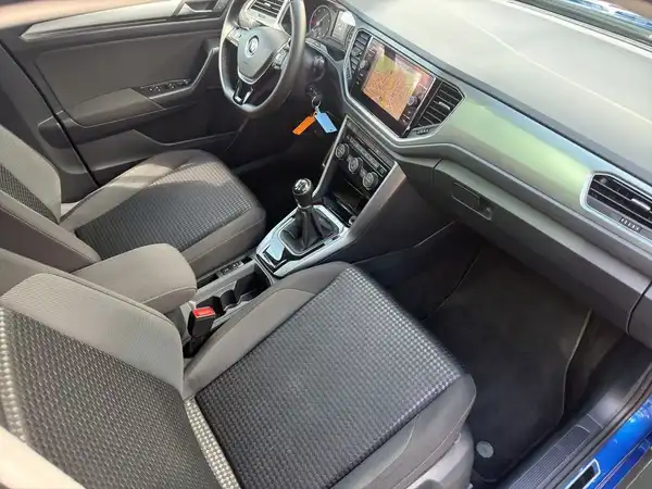 Das Bild zeigt das Innere eines blauen VW T-Roc mit grauen und schwarzen Stoffinterieur. Die Aufnahme ist von vorne, auf die Sitze und das Cockpit gerichtet.