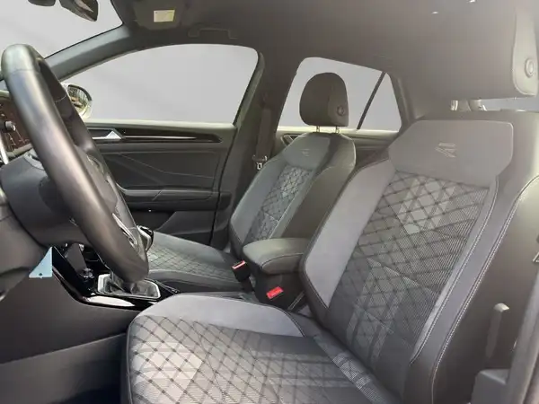 Das Bild zeigt den Innenraum eines VW T-Roc aus einer Innenansicht, mit schwarz-gemusterten Sitzen und einem modernen Armaturenbrett.