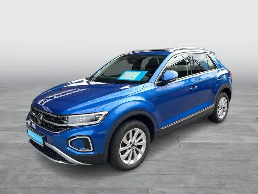 Das Bild zeigt einen VW T-ROC aus der Seitenansicht in blauer Farbe, mit markanten Texteinblendungen.