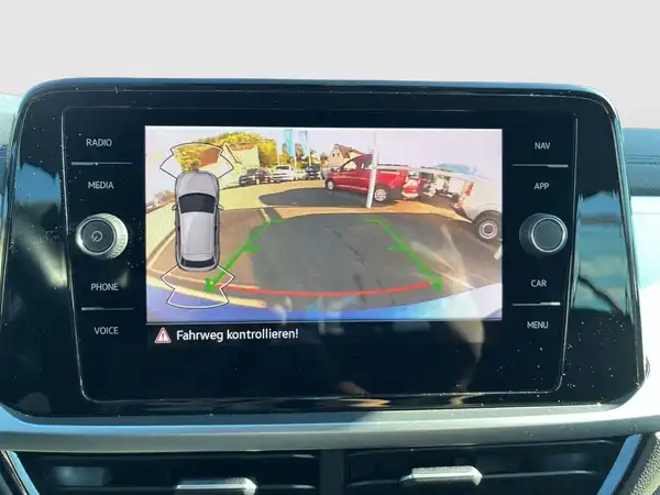 Das Bild zeigt die Innenaufnahme des Fahrzeugs, insbesondere das Display des Navigationsgeräts mit einer Rückfahrkameraansicht und einer Aufforderung zur Kontrolle des Fahrwegs.