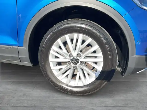 Das Bild zeigt die Seite eines blauen VW T-ROC, insbesondere das Rad und die Felge.