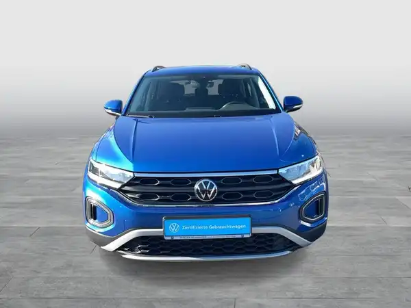 Das Bild zeigt einen VW T-Roc aus der Frontalansicht in blauer Farbe. Es enthält ein Händelrslogo und markante Texteinblendungen.