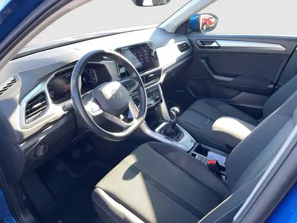 Das Bild zeigt das Innere eines blauen VW T-ROC mit schwarzem Interieur. Die Aufnahme ist von vorne in das Fahrzeuginnere gerichtet.