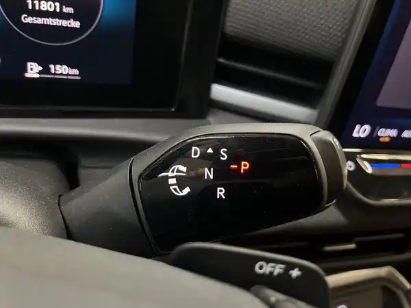 Das Bild zeigt das Schaltteil eines VW T-ROC im Innenraum mit einem schwarzen Interieur und markanten Texteinblendungen.
