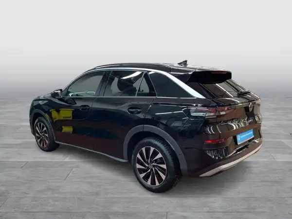Das Bild zeigt einen schwarzen VW T-ROC von der Seite, aufgenommen in einem modernen Studio mit neutralem Hintergrund.
