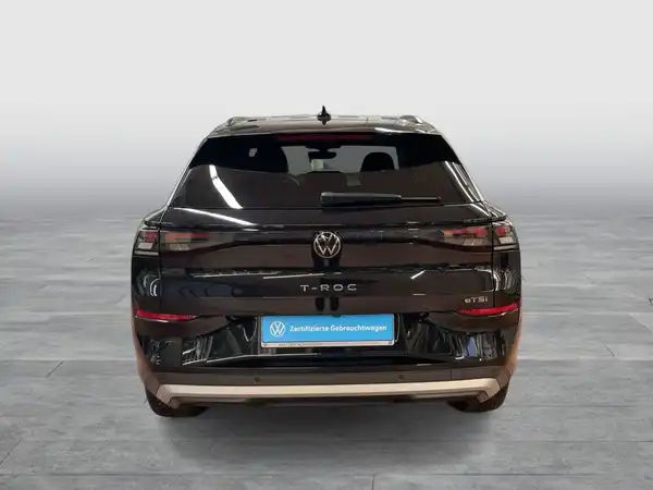 Ein Bild eines schwarzen VW T-Roc, aufgenommen von hinten. Es ist ein Fahrzeugbild mit Händlerlogo und markanten Texteinblendungen.