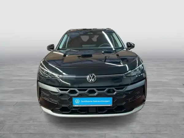 Das Bild zeigt einen schwarzen VW T-ROC aus der Frontansicht. Auf dem Foto ist das Händlerlogo eingeblendet und es enthält markante Texteinblendungen.