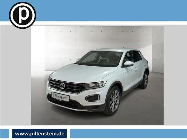 Das Bild zeigt einen weißen Volkswagen T-Roc aus der Frontalansicht. Es enthält das Händlerlogo und eine markante Texteinblendung mit der Website www.pillenstein.de.