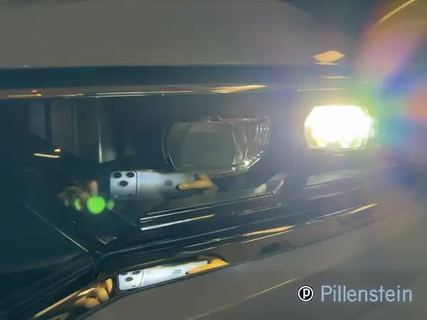 Nahaufnahme der Scheinwerfer des VW T-ROC, aufgenommen von vorne, mit einem Händlerlogo im Bild.