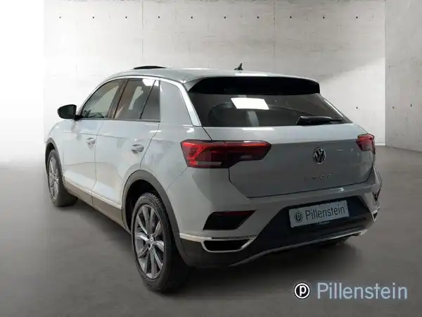 Das Bild zeigt einen silbernen VW T-ROC von hinten. Auf dem Foto ist das Händlerlogo "Pillenstein" eingeblendet.