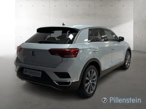 Das Bild zeigt einen silbernen VW T-Roc von hinten. Das Händlerlogo "Pillenstein" ist eingeblendet.