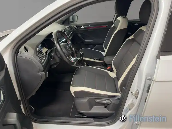 Das Bild zeigt das Innere eines VW T-ROC in Silber, mit schwarzen Sitzen und weißen Akzenten. Es handelt sich um eine Innenaufnahme des Fahrzeugs.