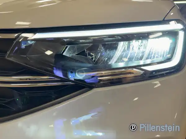 Das Bild zeigt den Scheinwerfer eines weißen VW Taigo, aufgenommen von vorne. Ein Händlerinformation ist im Bild enthalten, jedoch keine auffälligen Texteinblendungen.