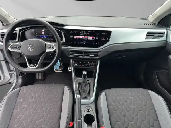 Das Bild zeigt das Innere eines VW Taigo. Der Blickwinkel ist auf das Armaturenbrett und die Sitze gerichtet. Die Innenfarbe ist schwarz mit grauen Akzenten.