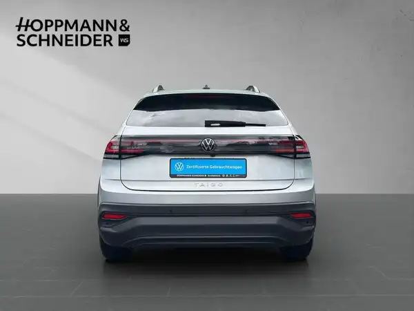 Das Bild zeigt einen silbernen Volkswagen Taigo von hinten. Im Bild ist ein Händlerinformationenlogo zu sehen.