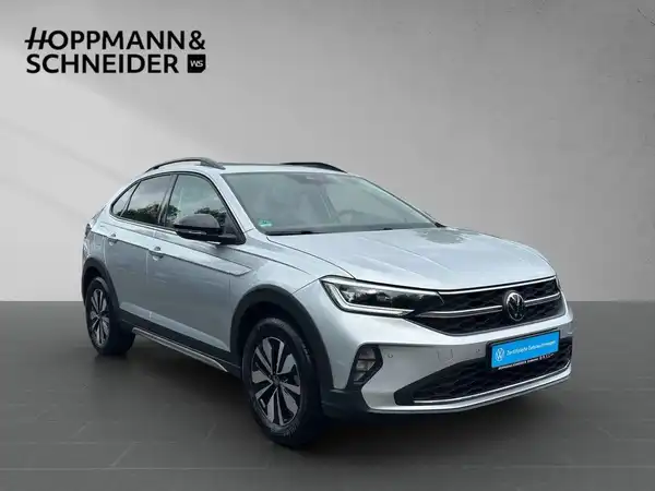 Das Bild zeigt einen silbernen VW Taigo von der Seite. Auf dem Foto ist das Händlerlogo Hoppmann & Schneider eingeblendet.