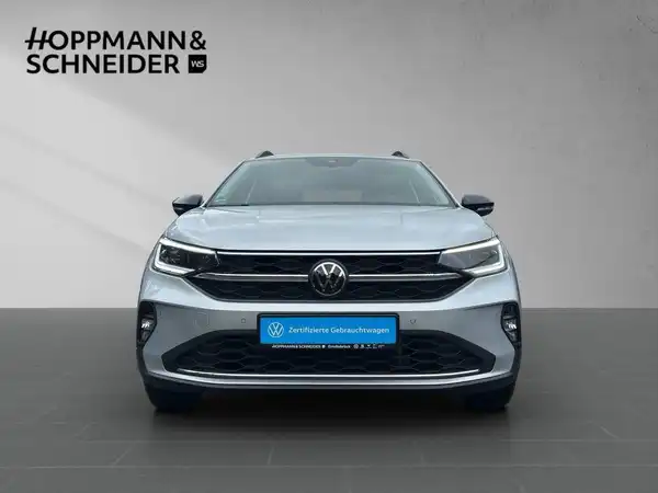 Das Bild zeigt einen silbernen VW Taigo von vorne. Das Händlerlogo von Hoppmann & Schneider ist auf dem Bild eingeblendet, sowie markante Texteinblendungen.