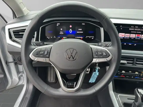 Das Bild zeigt das Inneninterieur eines VW Taigo mit schwarzem Lenkrad und Armaturenbrett. Der Blickwinkel ist auf das Lenkrad und die Instrumententafel gerichtet.