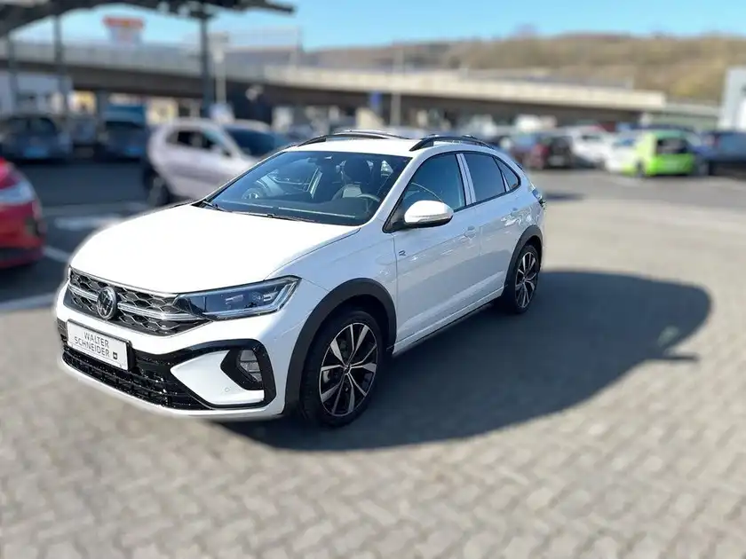 Das Bild zeigt einen weißen VW Taigo R-Line, aufgenommen von der Seite in einem Parkplatzbereich.