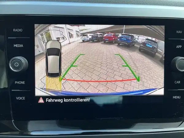 Das Bild zeigt den Innenraum des Fahrzeugs mit einem Rückfahrkamera-Display. Es enthält einen Text "Fahrweg kontrollieren!".
