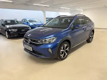 Das Bild zeigt einen blauen VW Taigo aus seitlicher Ansicht in einer Verkaufsfläche.