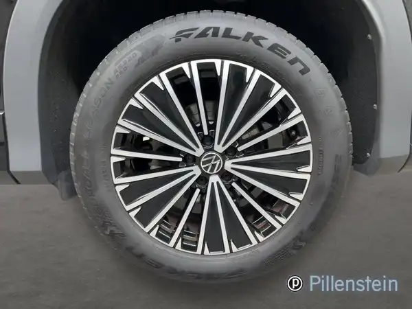 Das Bild zeigt das Innere eines VW TAYRON, aufgenommen aus der Perspektive des Fahrers. Das Interieur ist grau mit schwarzen Akzenten und es sind markante Texteinblendungen sowie ein Händlerlogo zu sehen.
