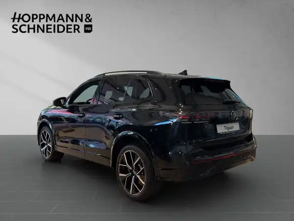 Das Bild zeigt einen schwarzen VW Tiguan von hinten. Im Hintergrund befindet sich das Händlerlogo 'HOPPMANN & SCHNEIDER'.