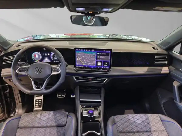Das Bild zeigt das Innere eines Volkswagen Tiguan mit einem modernen Armaturenbrett, einem großen Bildschirm und einer stilvollen Sitzgestaltung in schwarz mit blauen Akzenten.
