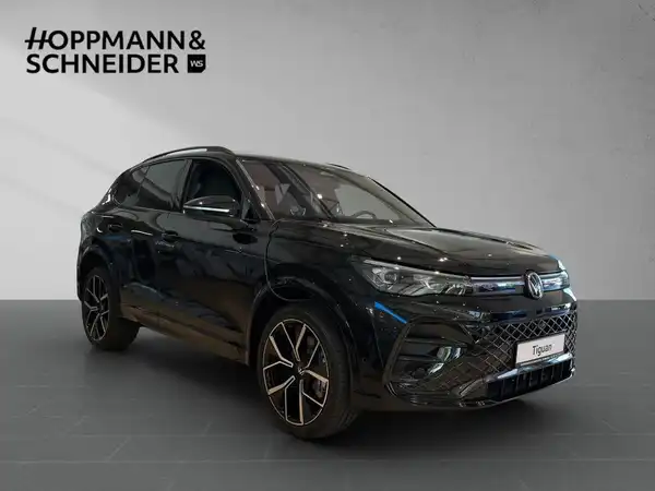 Das Bild zeigt einen schwarzen VW Tiguan aus seitlicher Perspektive. Im Hintergrund ist das Händlerlogo HOPPMANN & SCHNEIDER sichtbar.
