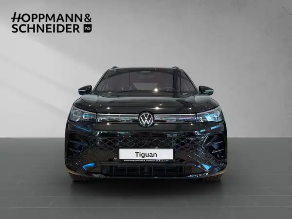 Das Bild zeigt einen schwarzen VW Tiguan aus der Frontalansicht. Oben links ist das Händlerlogo sichtbar und es gibt eine Texteinblendung mit dem Modellnamen "Tiguan".