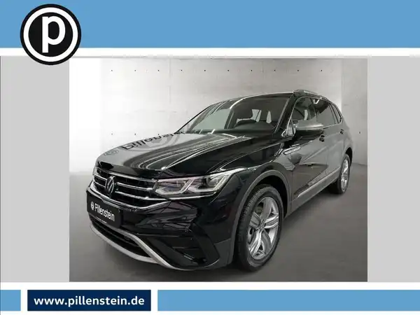 Das Bild zeigt einen VW Tiguan Allspace, aufgenommen von der Seite. Das Fahrzeug hat die Farbe Schwarz. Auf dem Foto ist das Händlerlogo von Pillenstein sichtbar und enthält markante Textelemente.