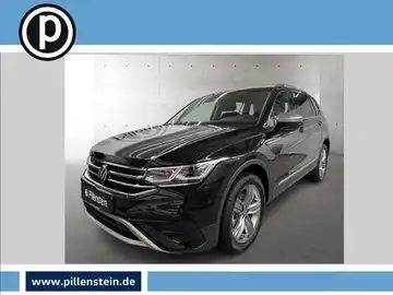 Das Bild zeigt einen VW Tiguan Allspace, aufgenommen von der Seite. Das Fahrzeug hat die Farbe Schwarz. Auf dem Foto ist das Händlerlogo von Pillenstein sichtbar und enthält markante Textelemente.