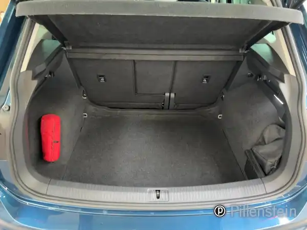 Das Bild zeigt den Kofferraum eines blauen VW Tiguan von hinten, mit einem roten Gegenstand darin. Das Händlerlogo ist sichtbar.