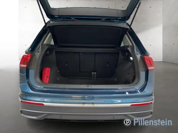 Das Bild zeigt den Kofferraum eines blauen VW Tiguan von hinten. Das Fahrzeug ist sichtbar, die Heckklappe ist geöffnet und der Innenraum des Kofferraums ist zu sehen.
