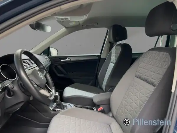 Das Bild zeigt das Innere eines VW Tiguan. Der Innenraum ist in Schwarz und Grau gehalten, und es sind zwei Sitze zu sehen.