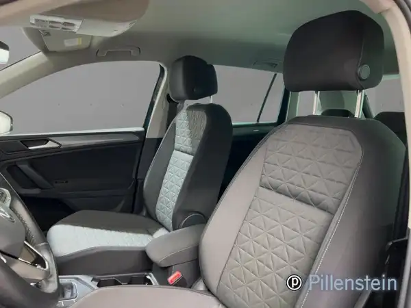 Das Bild zeigt das Innere eines VW Tiguan mit schwarzen und grauen Sitzen. Das Händlerlogo ist sichtbar.