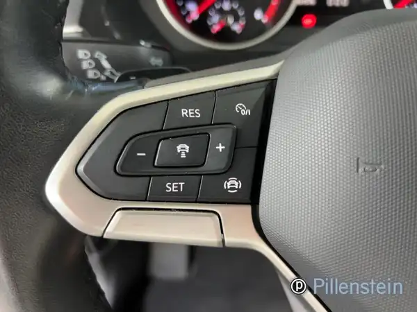 Das Bild zeigt das Innere eines VW Tiguan mit einem Fokus auf das Lenkrad und die Bedienelemente. Die Innenfarbe ist schwarz und es gibt ein Händlerlogo.