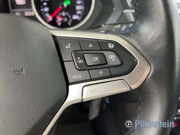 Das Bild zeigt das Lenkrad und die Bedienelemente im Innenraum eines VW Tiguan. Der Innenraum ist schwarz.