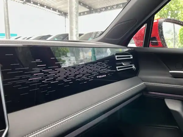 Innenansicht des VW Tiguan, zeigt das Armaturenbrett in schwarzer Farbe mit markanter Texteinblendung 'TIGUAN'.