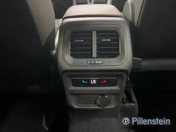 Das Bild zeigt eine Innenaufnahme des VW Tiguan Allspace. Es ist das zentrale Bedienfeld mit Klimaregelung zu sehen, farblich schwarz. Zusätzlich ist das Händlersymbol von Pillenstein eingeblendet.