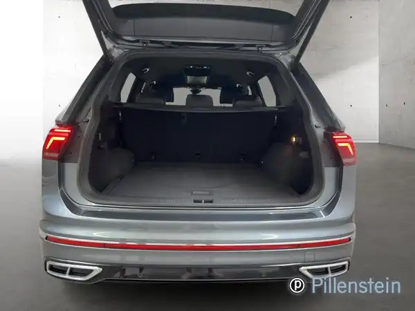 Das Bild zeigt den Kofferraum eines VW Tiguan Allspace von hinten. Das Fahrzeug ist grau, und das Händlerlogo von Pillenstein ist eingeblendet.