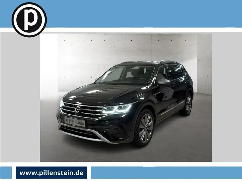Das Bild zeigt einen schwarzen VW Tiguan Allspace frontal aufgenommen. Das Händlerlogo ist vorhanden und es gibt markante Texteinblendungen.