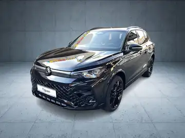 Das Bild zeigt einen schwarzen VW Tiguan aus der Frontansicht. Es sind markante Texteinblendungen und ein Händlerlogo sichtbar.