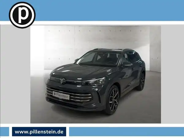 Das Bild zeigt einen grauen VW Tiguan von vorne. Es ist ein Fahrzeugbild mit Händlerinformationen und Logo im oberen linken Eck.