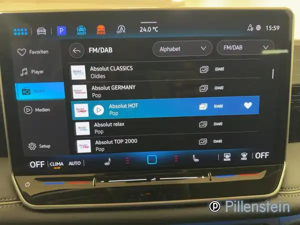 Blick ins Innere des Fahrzeugs, zeigt das Infotainment-System mit Radiostationen, das Interieur ist schwarz und es gibt ein Händlerlogo.