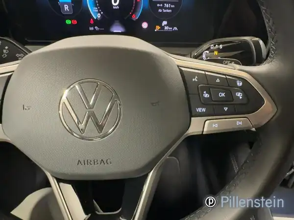 Das Bild zeigt das Lenkrad und das Armaturenbrett eines VW Tiguan aus einer Innenaufnahme. Das Interieur ist in Schwarz gehalten und es ist ein Händlerlogo sichtbar.
